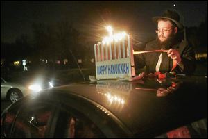 Other cars arrive as Tzemach Shemtov fastens a menorah to the rooftop before the beginning of the third annual Chanukah Menorah Car Parade near Chabad House in Toledo.