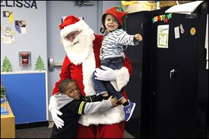 Santa Claus, played by William Smith with the UAW, holds Jett Reynolds, 2, right, and he gets a hug from DeAndre Patterson, 5, left, while visiting the children of Toledo Day Nursery.