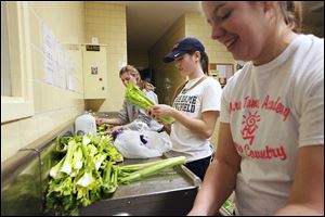Natalie Walter, 16, Erin Schaefer, 17, and Emily Currier, 16, from left, share a laugh while washing celery to be used in the dishes to be taken to Kentucky. 