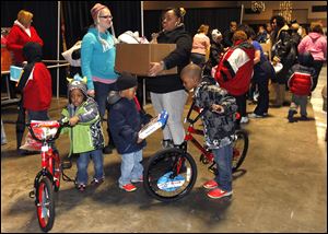 Shannan Upchurch holds a box of giveaway items as her boys, Malik, 5, center, and Michael, 6, right look at their new toys from the Noel Project. At left is Jaron Smith, 3.