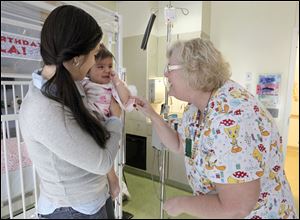 Toledo Hospital nurse Pattye Nicolls, right, greets Ayla Soria, 1, while she is with her mother Angalina Soria in the Debbie Brass Children's Cancer Center earlier this month.