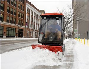 City worker Bryan Davis clears the Huron Street sidewalk of snow, today, in downtown Toledo.