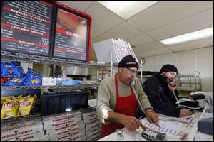 Bambino’s Pizza co-owner Hassan Awada, left, and manager Tynan Rubin field two phone lines Monday to take pizza orders from customers who didn’t want to venture out into the cold for food.