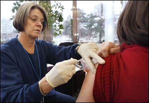 Nurse Mary Sheehy gives a flu vaccine injection to Megan Vahey Casiere, chief of planning and development for Lucas County, at One Government Center in Toledo.