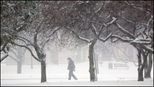 A lone pedestrian braves the snowfall on Jackson Street in Toledo. Temperatures Sunday reached 24 degrees, but they’re expected to plunge to dangerous levels today through the middle of the week.