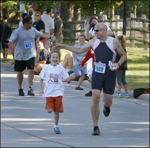 Joey Boyle, 8, left, joins his father, Joe Boyle, for the last 50 yards of Sylvania Triathlon/Duathlon in Sylvania in August. Mr. Boyle wants to cross the finish line before he starts a new round of chemotherapy treatments.