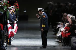 Toledo Fire Chief Luis Santiago salutes the casket of James Dickman as Private Dickman’s wife, Jamie, right, holds their daughter Paige.