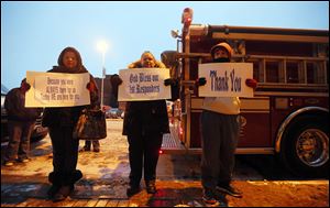 Toledoans Arianna Hudson, left, Sherry Ruiz, center, and Pete Ruiz brave the cold to honor firefighters outside of the SeaGate Convention Centre as mourners file past to go to the Last Alarm service for Stephen Machcinski and James Dickman.