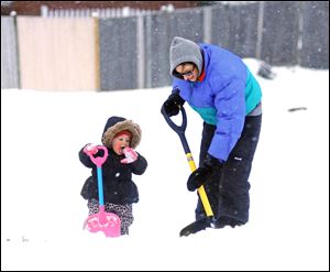While Lauren Berthiaume, right, shovels her sidewalk, her 17-month-old daughter Rylie Bartusek prefers eating the snow, Wednesday in Worcester, Mass.