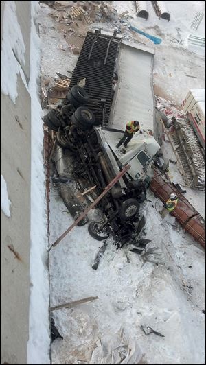 Emergency crews examine the wreckage after a collision between a car and a tractor-trailer sent the rig careening off the bridge from northbound I-475 onto Manley Road in Maumee.