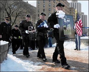 A Pittsburgh police officer leads the memorial procession with a photo of fallen police dog Rocco on the steps of the Soldiers and Sailors Memorial Hall and Museum in Oakland, Pa.