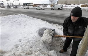 Sam Elseyed, employee of All Pro Quick Lube, shovels the snow and ice on the business’ Secor Road front after a city inspector stopped by on Tuesday.