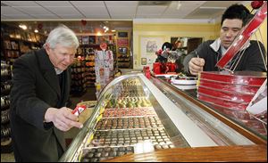 Bruce Brodbeck of Toledo selects chocolate pieces for his wife at Maumee Valley Chocolate and Candy shop in Maumee on Wednesday as shop co-owner Jason Sieminski helps him.
