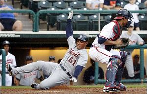 The Tigers' Ezequiel Carrera slides past Atlanta’s Christian Bethancourt to score what would become the winning run after a rain-delay was called in the ninth. 