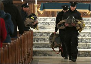 Toledo  firefighters carry two fire jackets, sets of  boots, and helmets during a memorial Mass for two fallen comrades at the Historic Church of St. Patrick.