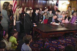 Ohio Gov. John Kasich signs a bill to grant school districts additional calamity days before a group of students at the Statehouse in Columbus.