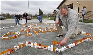 ABOVE: Kyle Schalow of Holland, right, and others build the RX Epidemic Memorial out of empty prescription drug bottles in Homecoming Park in Springfield Township. Mr. Schalow started the  RX Epidemic Memorial Foundation after his wife, April, at left in background, became addicted to prescription pain killers.