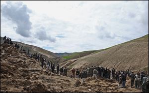 Survivors walk and search for their relatives' bodies today at the site of Friday's landslide.
