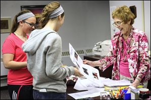 Alexis Waclawski, 16, left, and Caitlyn Schwiefert, 16, deliver an advance copy of the school newspaper to secretary Anita Shufritz, 73, in the Rossford High School office. She is retiring as school secretary after 56 years with the district and is featured in the student paper for her years of service.