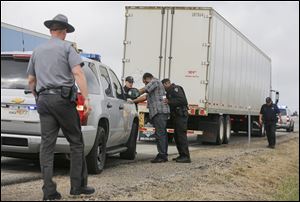 Trooper Will Richardson pats down the driver of a tractor-trailer as Troopers Ryan Stewart and Al Romero and Sgt. Kurt Beidelschies stand by along the Ohio Turnpike.