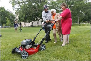 Sterling House of Bowling Green resident Trudy Price mows the he Bowling Green University Hall lawn in celebration of her 100th birthday with help from  Scott Euler, left, and Christine Burger, right.