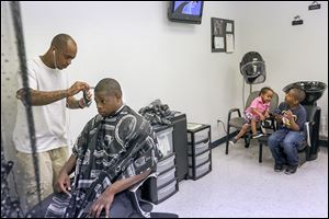 Barber Devon Hands, Sr., talks with Nathaniel Jenkins IV while trimming his hair as Mr. Hands’ son Da’Mauri, 2, and stepson Dale Richardson-Bey, 8, play. Groups providing the haircuts say looking good gives men confidence at work and at home. 