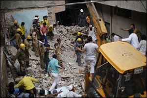 Indian rescuers gesture for an excavator to stop as they try to retrieve the body of a victim at the site of a building collapse in New Delhi, India.