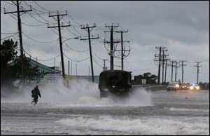 A military vehicle and a man navigate a flooded Highway 64 as wind pushes water over the road while Hurricane Arthur passes through Nags Head, N.C.