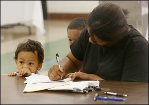 Nathan Barker, 2, and his brother Melvin, Jr., 4, center, keep close to their mother, Lisa, as she fills out forms during the recruitment fair for Toledo Public Schools’ preschool program at the former DeVilbiss High School.