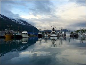 Fishing boats, reflected in the water, glow in the soft evening light at Valdez Harbor.