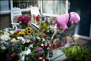 A woman lights a candle near flowers and candles placed in honor of three citizens, a mother, 17-year-old daughter and 13-year-old son who were among the victims of flight MH17 in Delft, Netherlands, today.