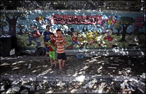 Palestinian boys stand next to wall with murals and Arabic writing that reads 