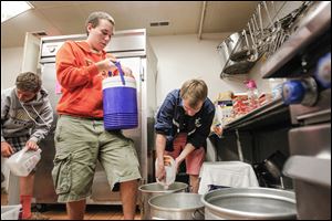 Tynan Hubbell, 14, left, of St. John’s High School, and BGSU students Aidan Hubbell-Staeble, 19, center, and Peter Funk, 20, pour out water from various containers at the Martin Luther King Center Kitchen for the Poor.