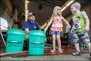 Clara Cousino, 4, center, and Clay Cousino, 2, right, both of East Toledo help firefighter Bryan West fill buckets at the fire station in Oregon.