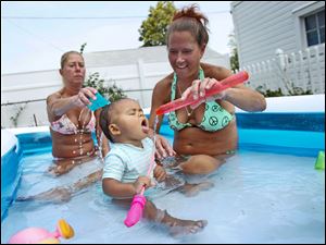 Connie Elter, left, and Dawn Szych, right, play with Myah Brown, center, 11 months, Szych's granddaughter, in a small pool at Szych's home in North Toledo Monday. Over the weekend, Brown received bottled water baths and today they decided to celebrate the clean water announcement Monday in the pool.