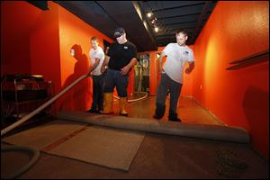Leanne Crosby,Tommy Meeks, and Nick Smallwood, from left, employees of Cousino-Harris Disaster Kleen-up, roll up the soaked carpet in the basement of the home of Jeff and Amy Bobak on Brook-haven Drive in  Perrysburg. Heavy rains flooded the basementsof homes  in parts of Perrysburg.