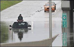 A stranded motorist sits on top his car as he awaits rescue from the flooded Southfield Freeway, Monday in Dearborn, Mich.