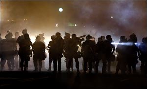 Police walk through a cloud of smoke as they clash with protesters Wednesday night in Ferguson, Mo.