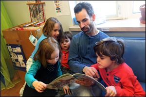 Clockwise from bottom left: sisters Alice and Sophie Rainey, 4, Isaac Proulx, 3, preschool teacher Dave Proulx and Adam Proulx, 5, read together at Mr. Proulx's classroom inside Bowling Green University's Jordan Family Development building.