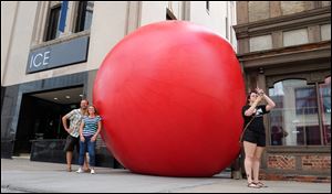 At left, RedBall artist Kurt Perschke poses with ICE Restaurant & Bar owner Donna Weisner for people taking pictures as Starr Jarvis takes a selfie with the Red Ball Wednesday on Madison Street in Toledo, Ohio.
