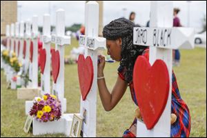 Santa Fe High School freshman, Jai Gillard writes messages on each of the 10 crosses in front of the school in Santa Fe. She was in the art class Friday morning and knew all of the victims of the shooting.
