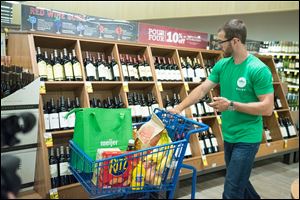 A Shipt personal shopper selects wine as part of a grocery order for a customer using home delivery.